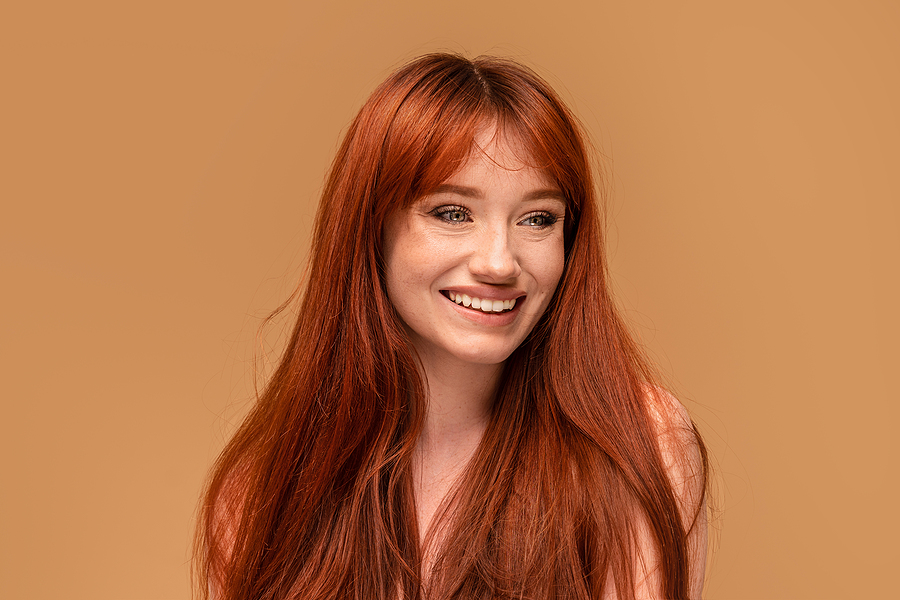 Authentic cheerful ginger girl with beautiful smile, natural freckles, long hair and fringe. Attractive red head woman posing in studio. A lot of copy space.